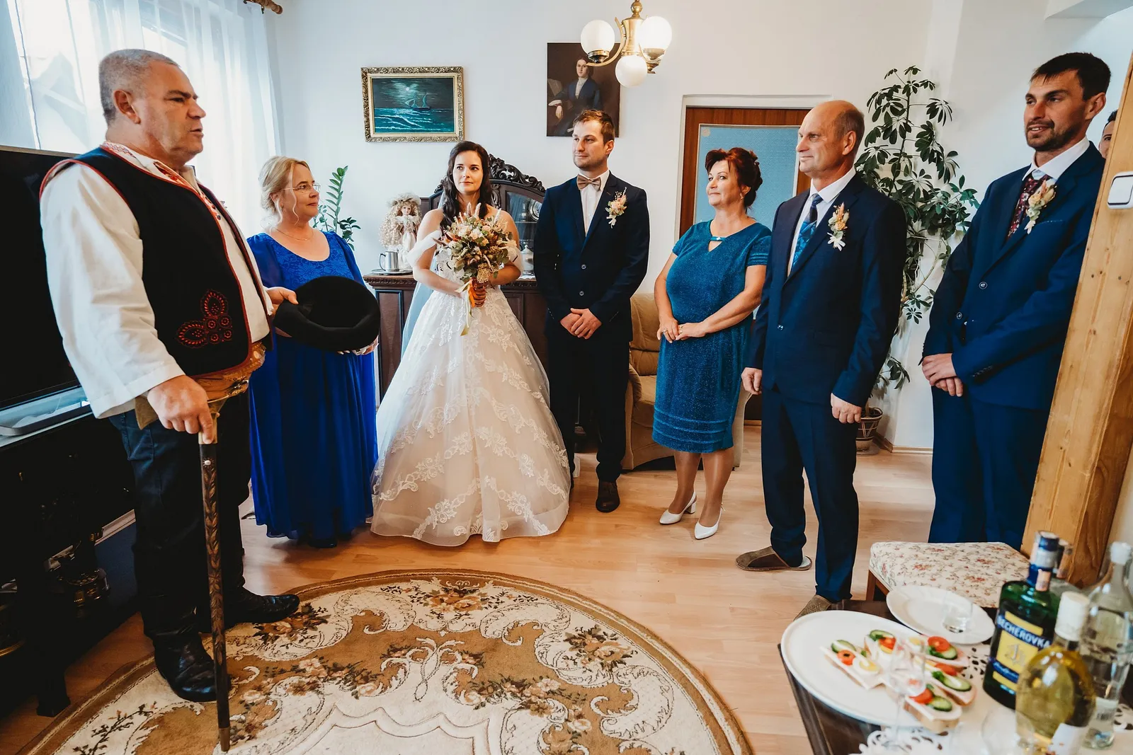 Širší záber na odobierku v izbe s okrúhlym kobercom, rodinou, svedkom a pohostením na stolíku – svadba Majka a Marek, Hotel Máj, Liptovský Ján