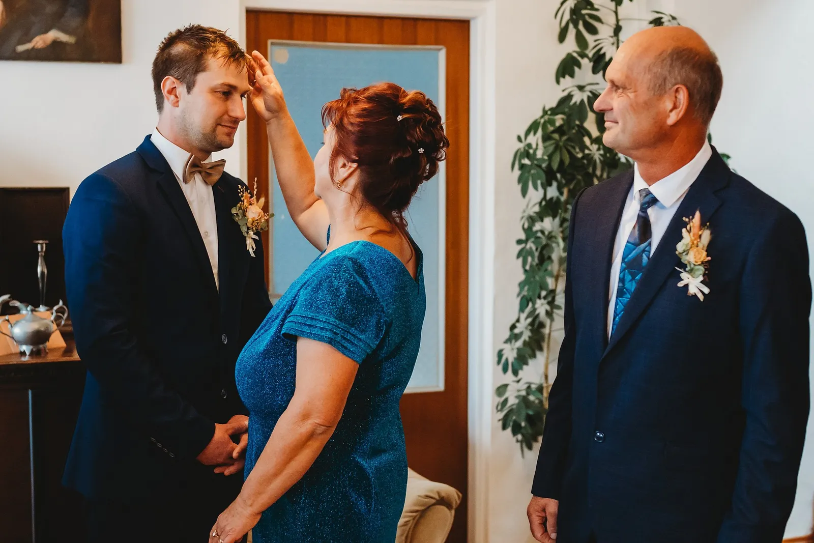 Žena v trblietavých modrých šatách žehná ženícha krížikom na čelo, vedľa sa usmieva muž v obleku – svadba Majka a Marek, Hotel Máj, Liptovský Ján