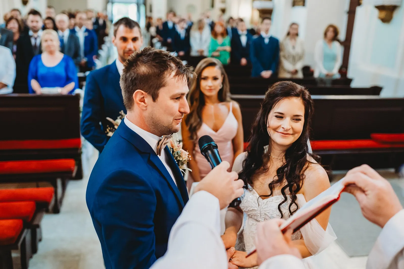 Nevesta sa usmieva počas sľubu, ženích jej drží ruky a kňaz mu podáva mikrofón a obradnú knihu – svadba Majka a Marek, Hotel Máj, Liptovský Ján