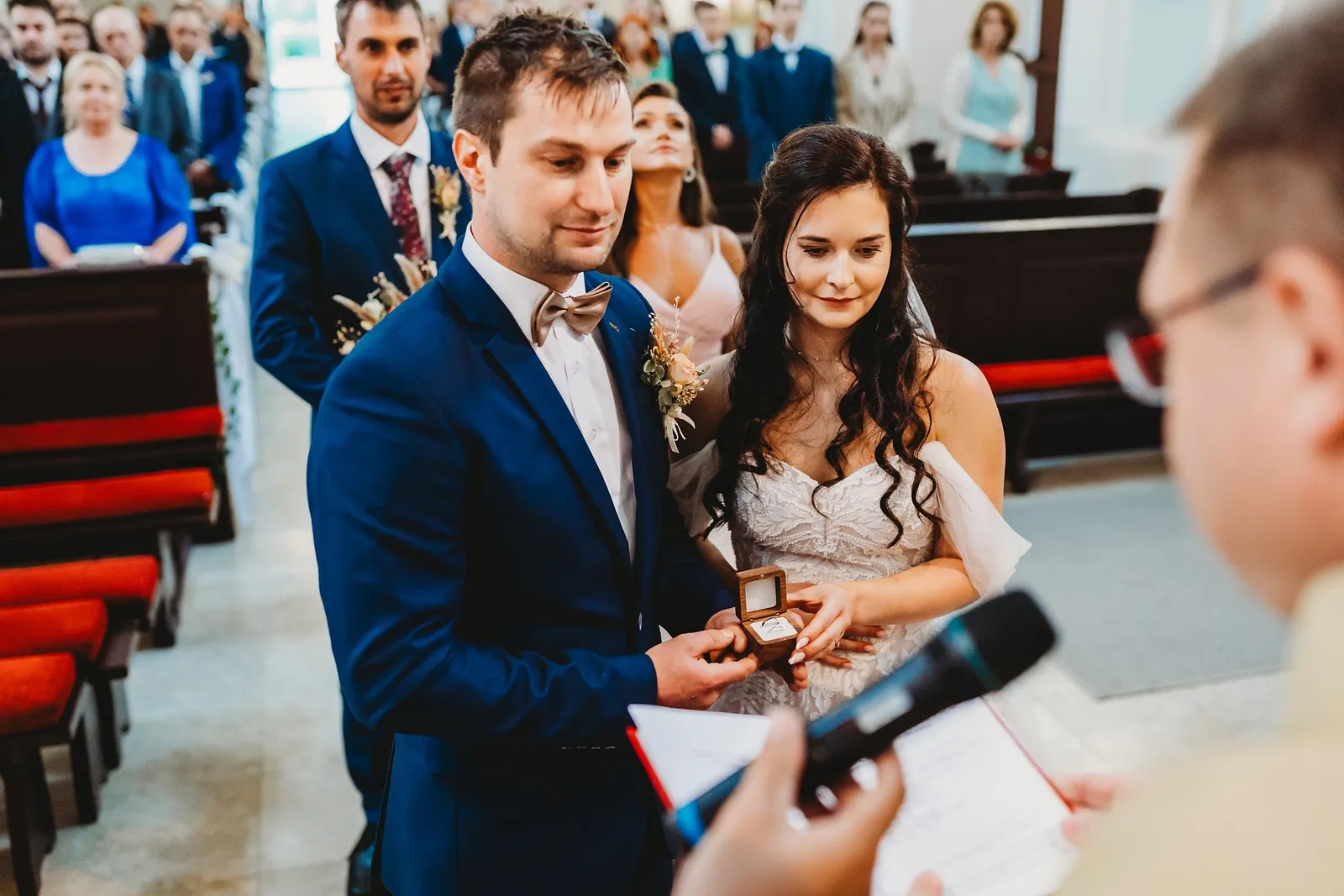 Nevesta a ženích držia otvorenú krabičku s obrúčkami pred kňazom s mikrofónom, za nimi svedkovia – svadba Majka a Marek, Hotel Máj, Liptovský Ján
