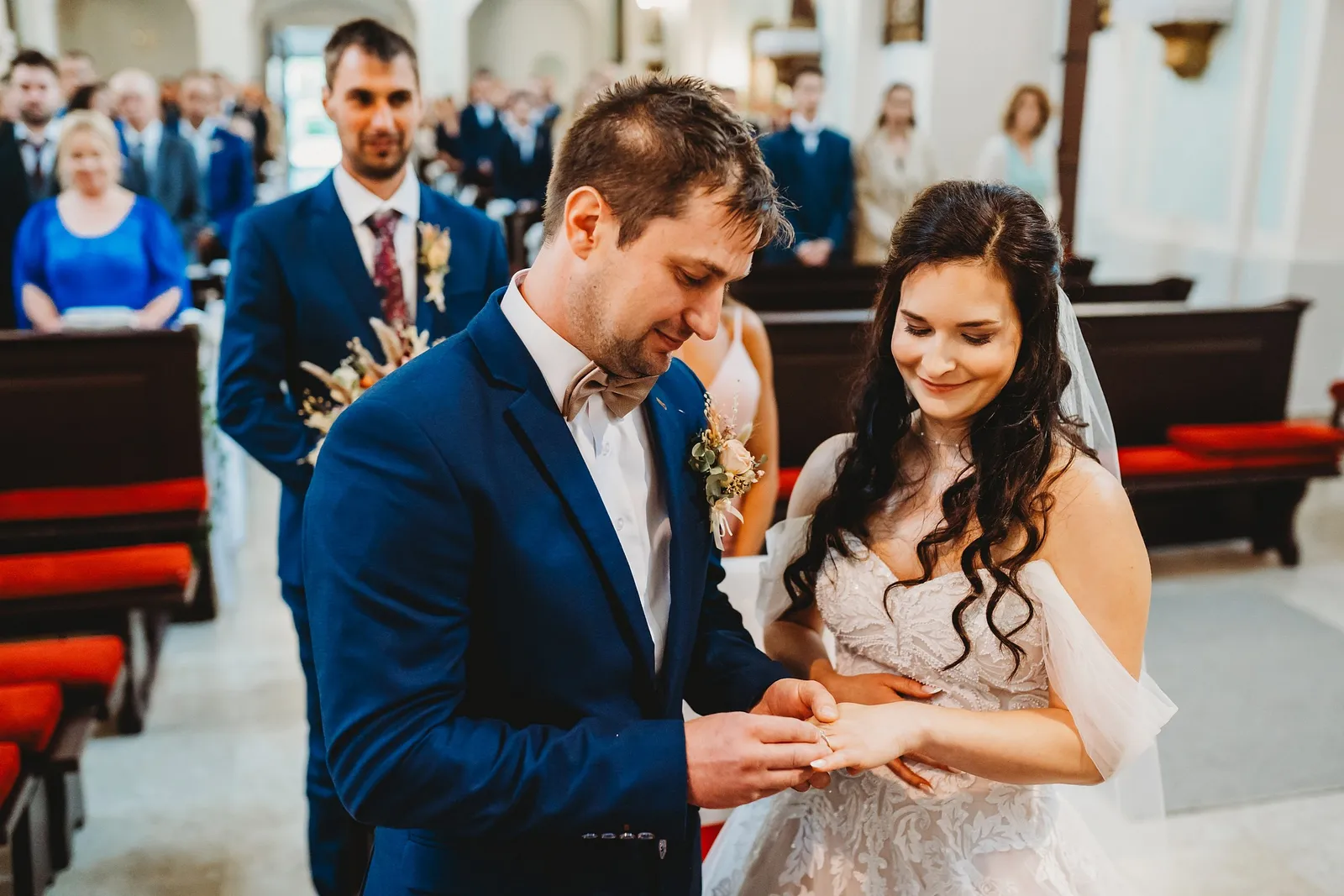 Ženích navlieka usmiatej neveste obrúčku na prst pred oltárom, v pozadí svedok a hostia – svadba Majka a Marek, Hotel Máj, Liptovský Ján