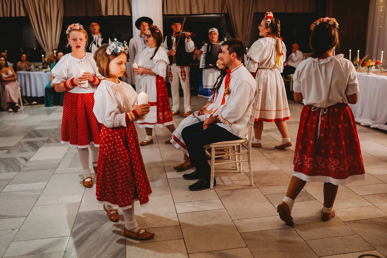 Dievčatá v červených krojoch so sviečkami obchádzajú sediacich novomanželov, hrá muzika – svadba Majka a Marek, Hotel Máj, Liptovský Ján