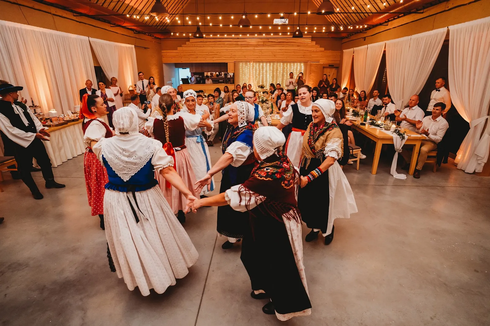 Ženy vo folklórnych krojoch a čepcoch tancujú v kruhu uprostred svadobnej sály – svadba Pajka a Majo, Stodola Liptovský dvor