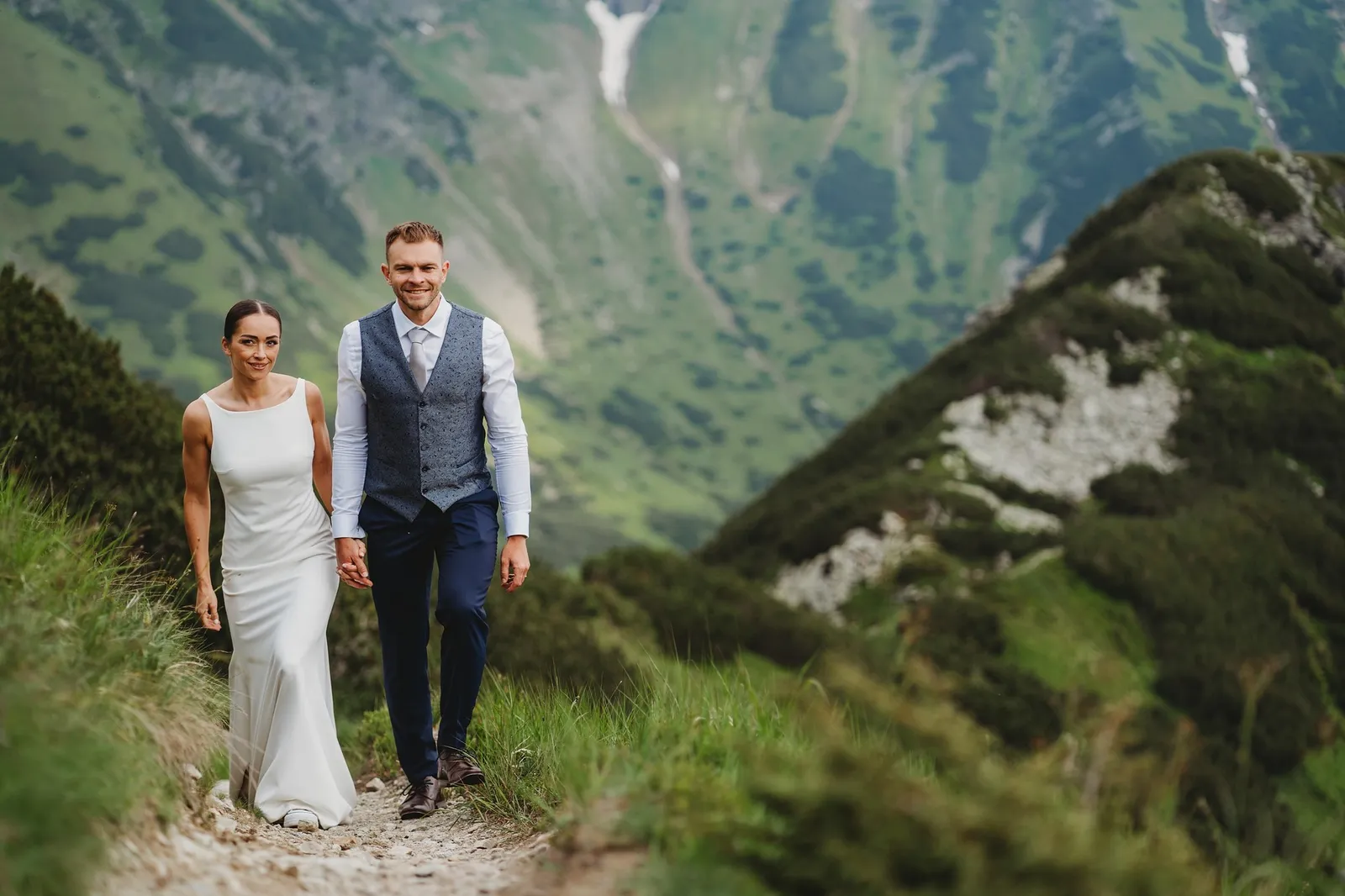 Usmiati novomanželia kráčajú ruka v ruke po úzkom chodníku na hrebeni Západných Tatier pod Smutným sedlom – svadba Pajka a Majo, Stodola Liptovský dvor