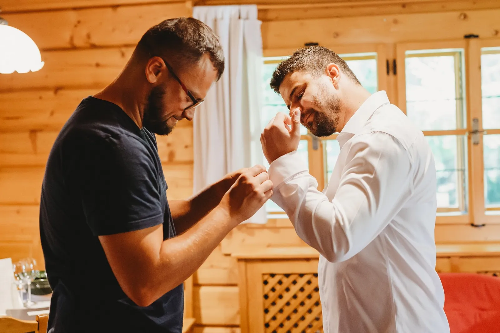 Kamarát v okuliaroch zapína ženíchovi manžety bielej košele v drevenej izbe – svadba Peťka a Peťo, Stodola Liptovský dvor