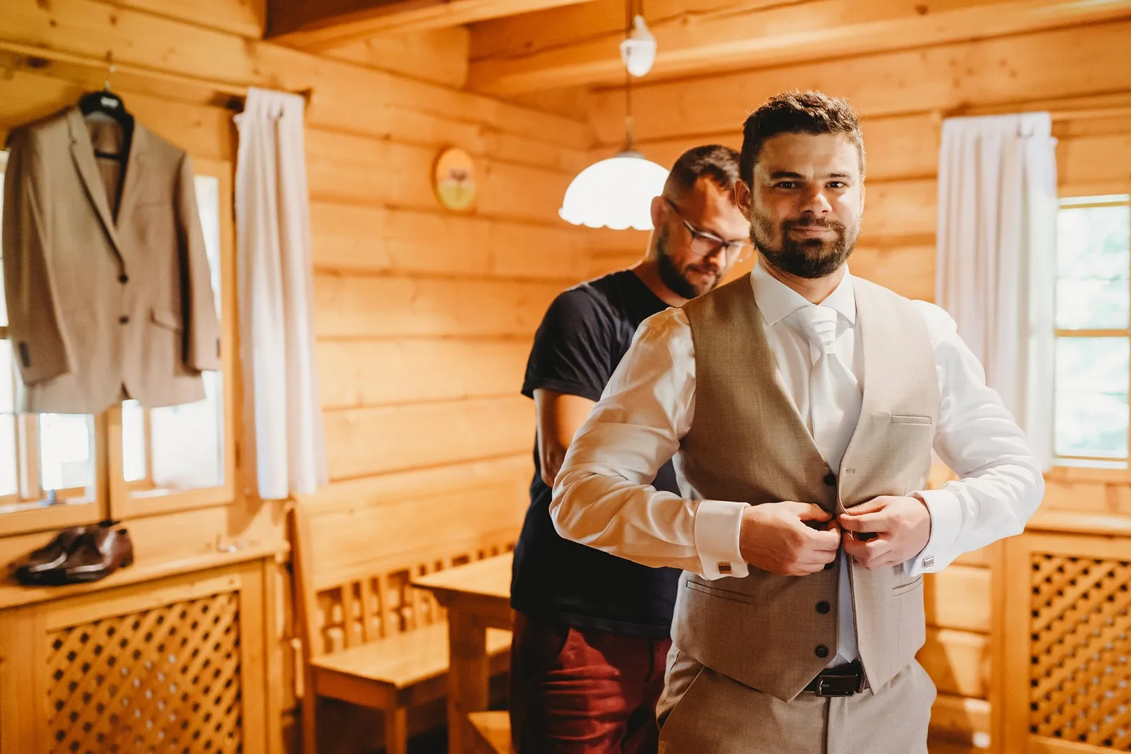 Usmiaty ženích si zapína béžovú vestu, za ním stojí kamarát v tmavom tričku – svadba Peťka a Peťo, Stodola Liptovský dvor