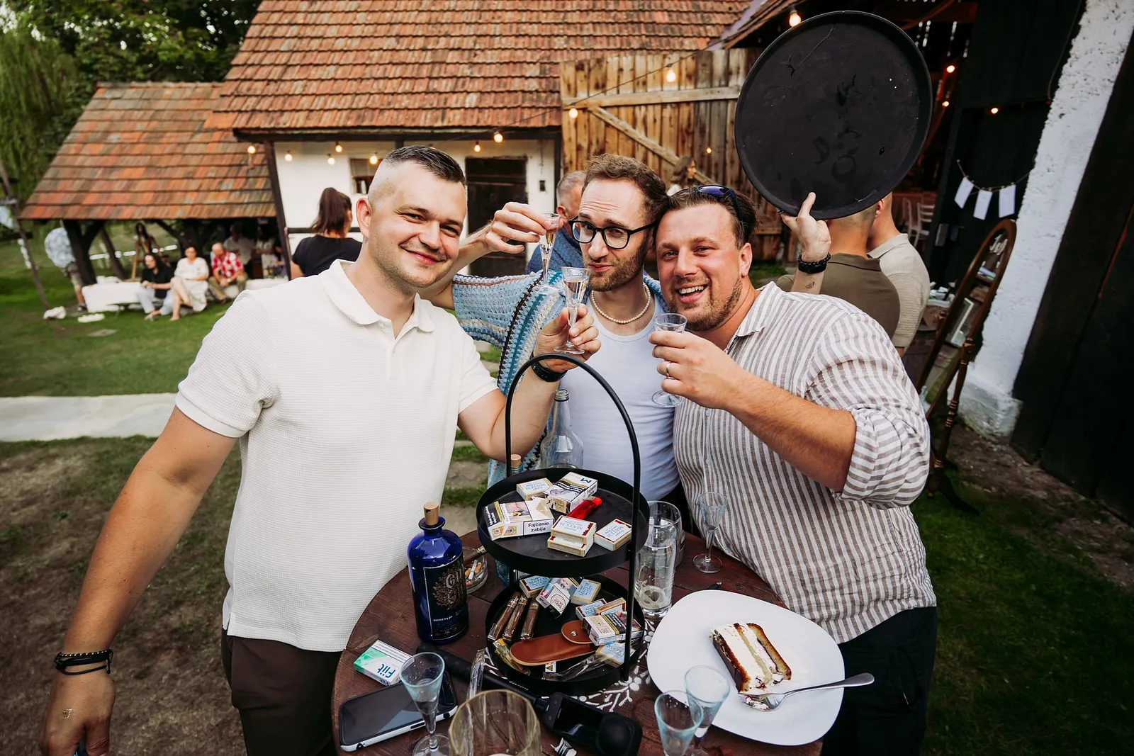 Traja hostia si pripíjajú pri stole s občerstvením na dvore pri stodole – svadba Ivka a Ondro, Humno Trnka, Záskov
