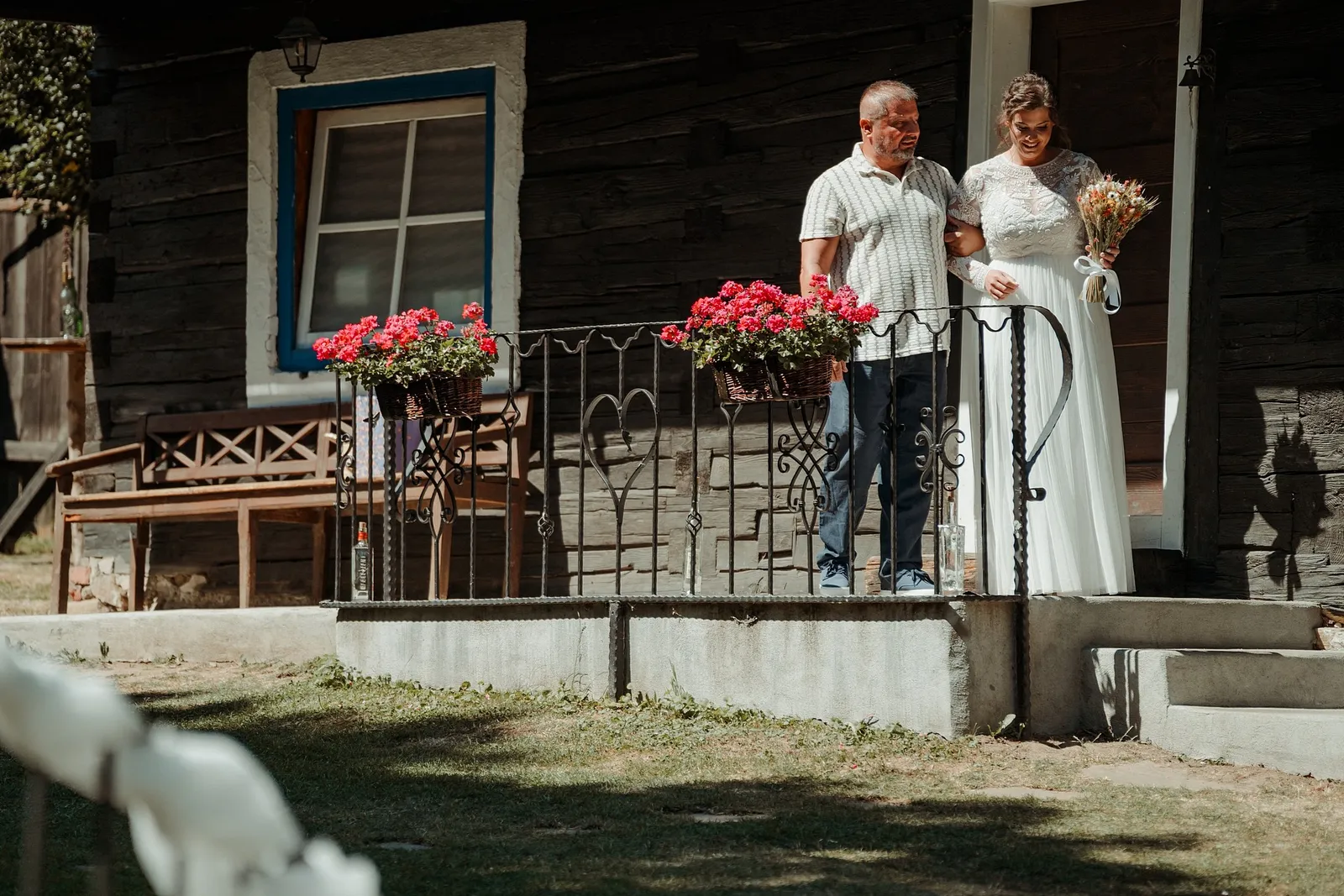 Nevesta s kyticou a jej sprievod stoja na schodoch drevenice s červenými muškátmi – svadba Ivka a Ondro, Humno Trnka, Záskov