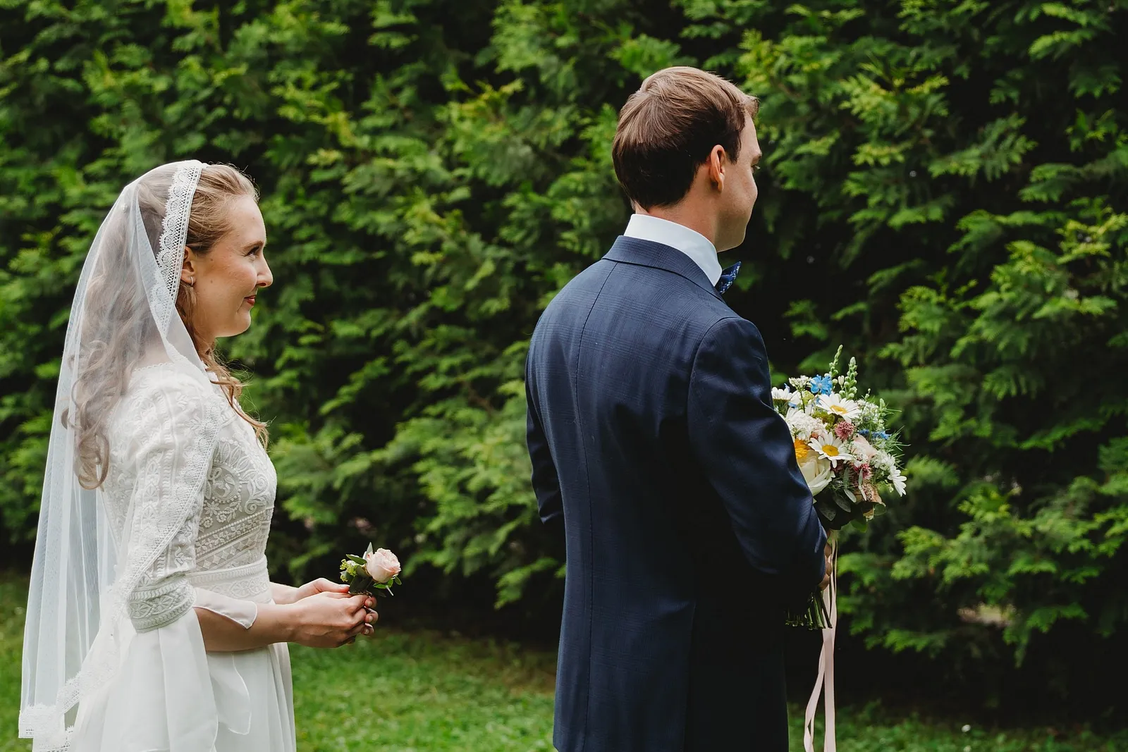 Nevesta v závoji s pierkom v ruke prichádza k ženíchovi otočenému chrbtom s kyticou – svadba Sandra a Sebastian, Stodola Gréta