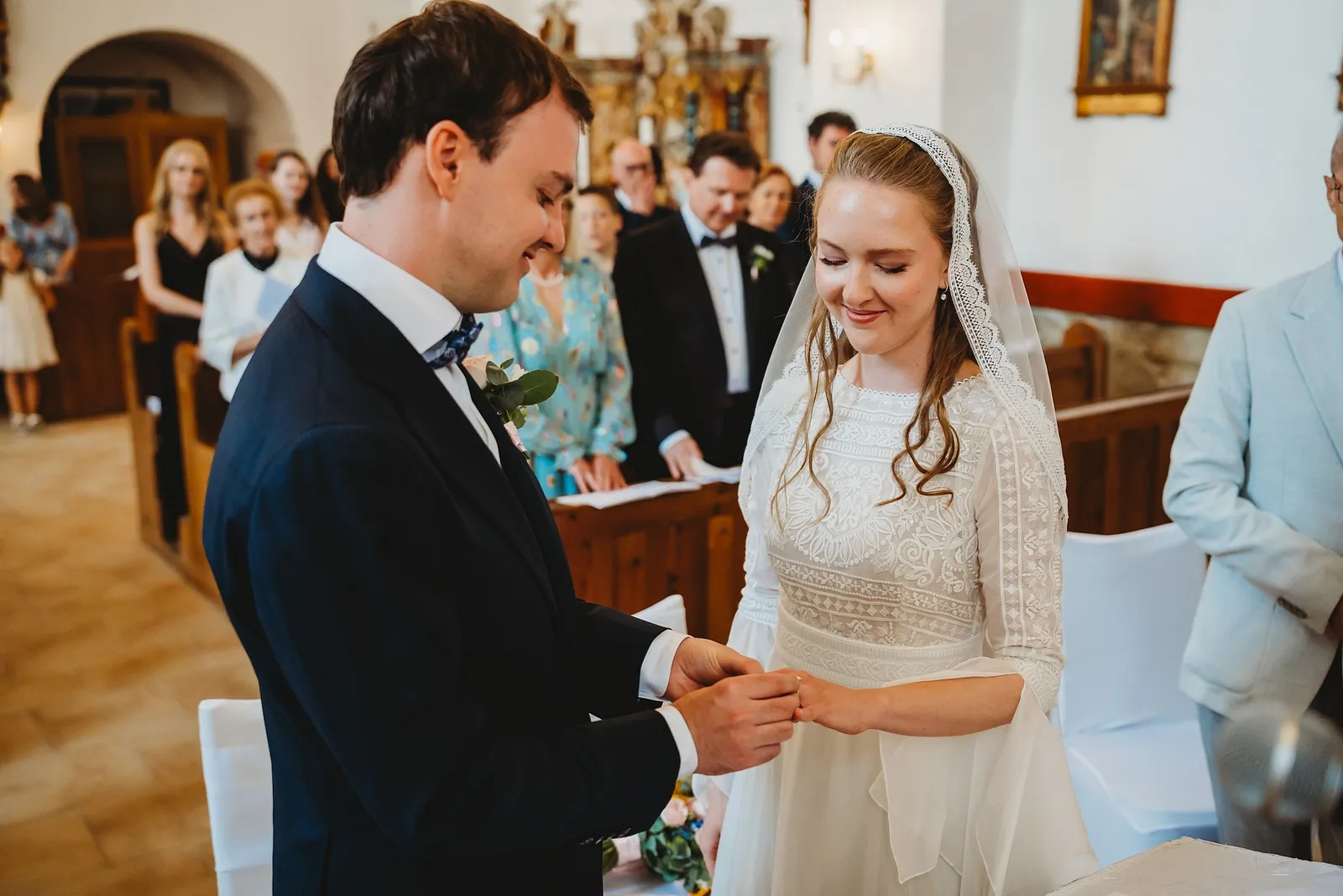 Nevesta sa šťastne usmieva, keď jej ženích navlieka obrúčku, v pozadí hostia v kostole – svadba Sandra a Sebastian, Stodola Gréta