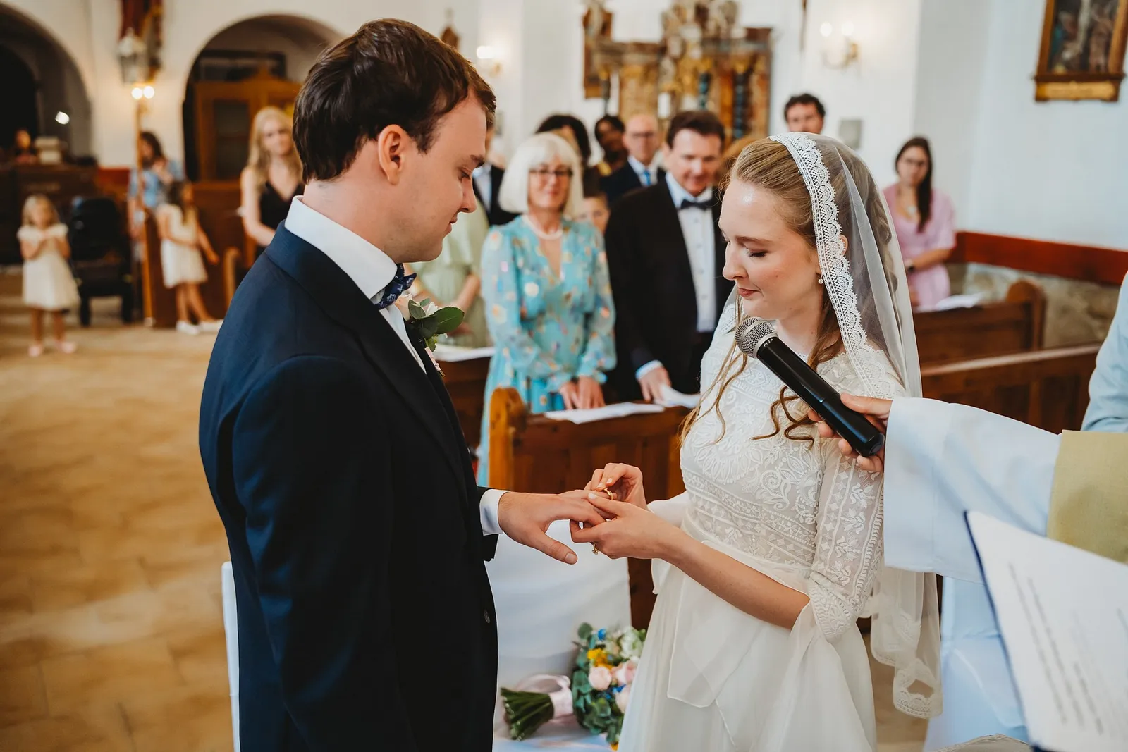 Nevesta navlieka ženíchovi obrúčku a hovorí do mikrofónu, ktorý jej podáva kňaz – svadba Sandra a Sebastian, Stodola Gréta