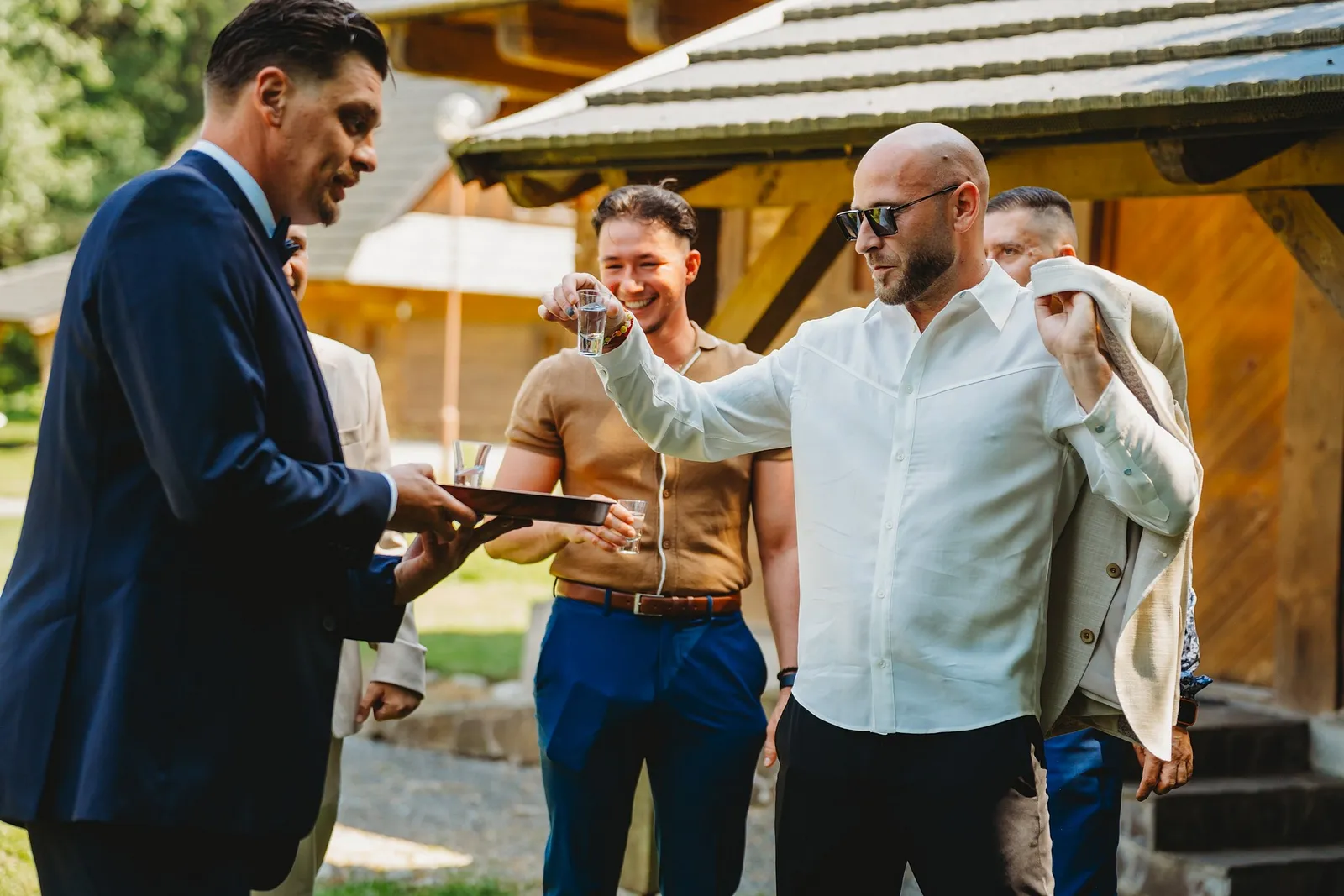 Muži si pred obradom pripíjajú pálenkou z podnosu pri drevenom altánku – svadba Simonka a Nuri, Stodola Liptovský dvor
