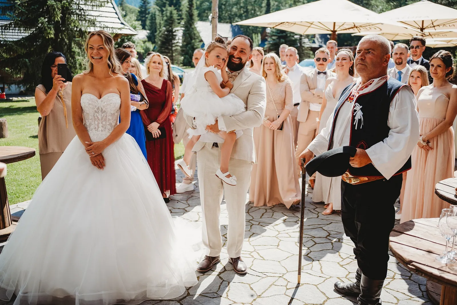 Ženích drží dievčatko na rukách, vedľa stojí nevesta a starejší v kroji – svadba Simonka a Nuri, Stodola Liptovský dvor