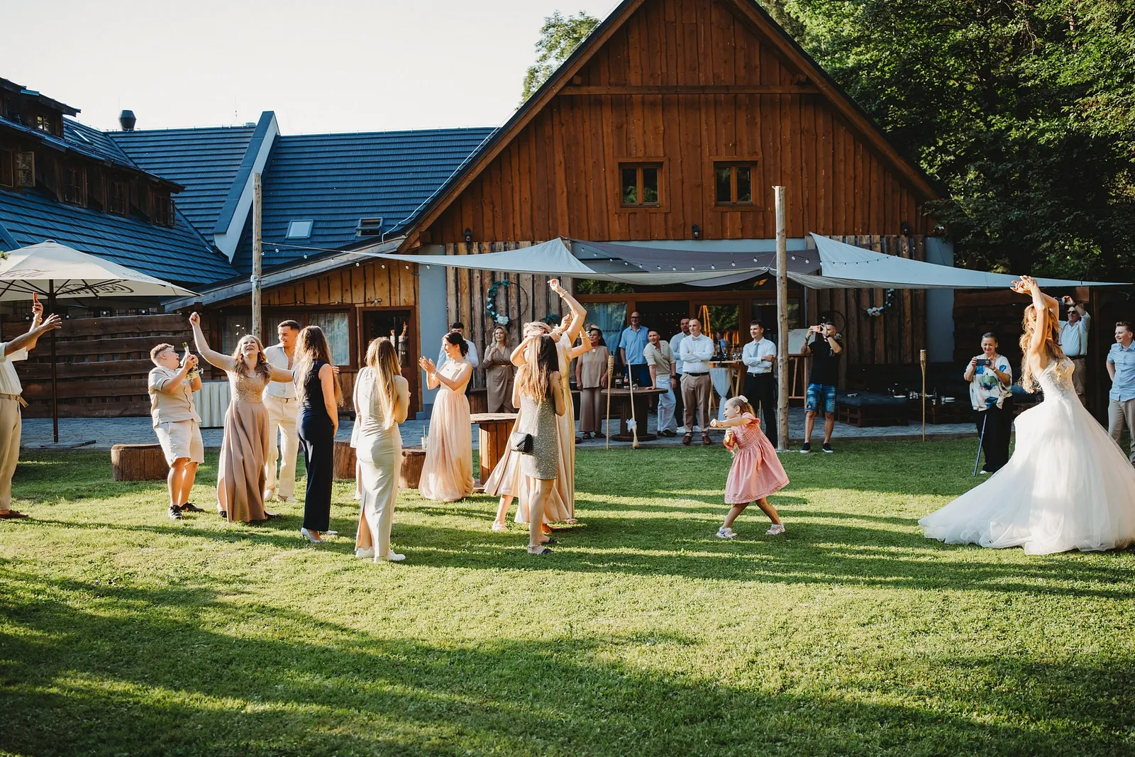 Ženy so zdvihnutými rukami čakajú na hodenú kyticu, medzi nimi dievčatko v ružovom – svadba Simonka a Nuri, Stodola Liptovský dvor