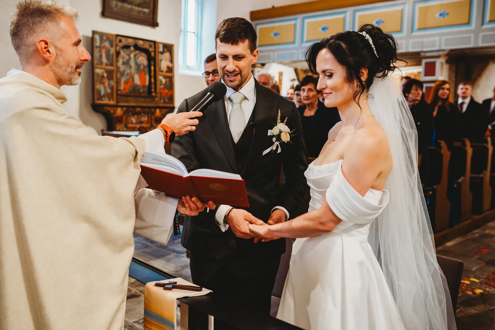 Ženích drží nevestu za ruku a hovorí manželský sľub do mikrofónu, ktorý drží kňaz – svadba Andrejka a Janko, Stodola Liptovský dvor