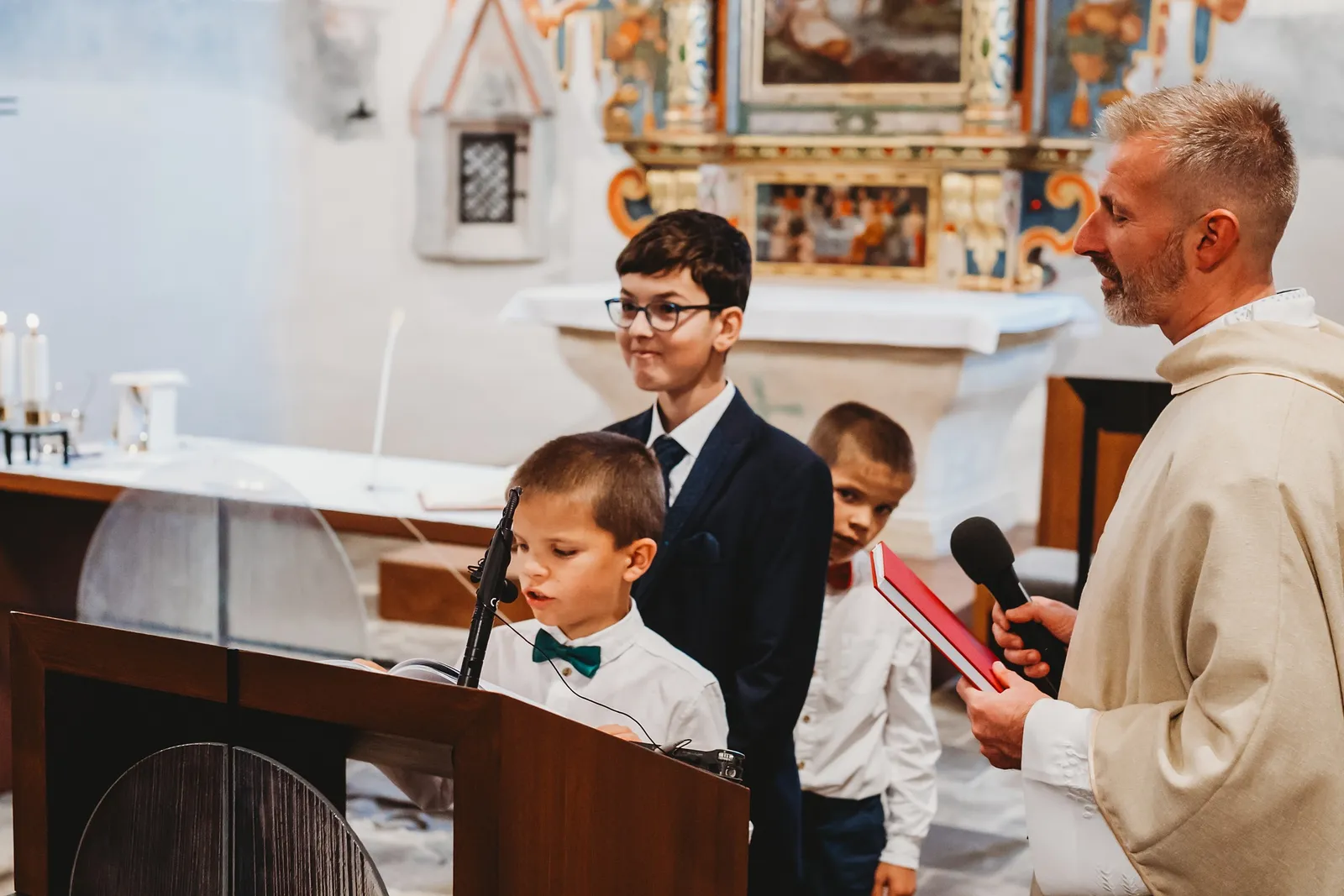 Traja chlapci v košeliach pri ambóne čítajú počas obradu, vedľa stojí kňaz s mikrofónom – svadba Andrejka a Janko, Stodola Liptovský dvor