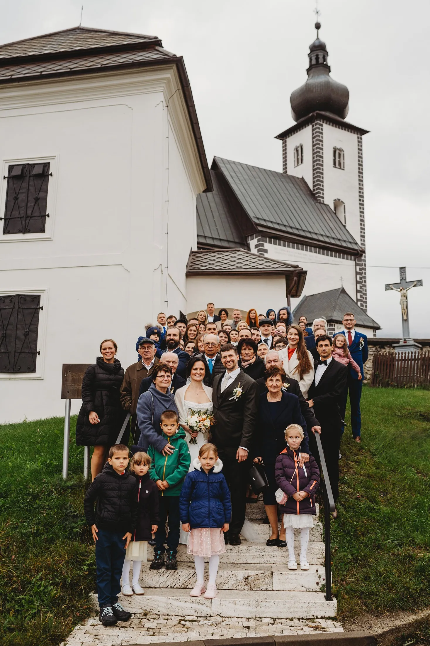 Spoločná fotka novomanželov so všetkými hosťami na schodoch pred bielym kostolom s vežou – svadba Andrejka a Janko, Stodola Liptovský dvor