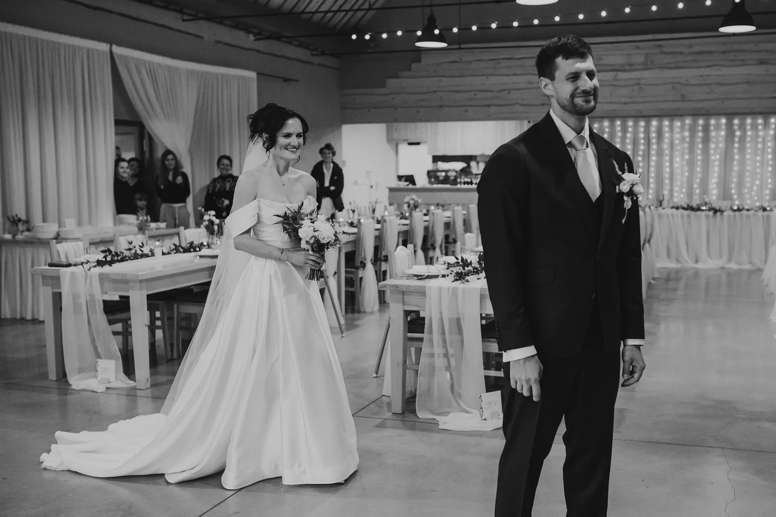 Čiernobiely first look, nevesta s kyticou sa usmieva za chrbtom čakajúceho ženícha v sále – svadba Andrejka a Janko, Stodola Liptovský dvor