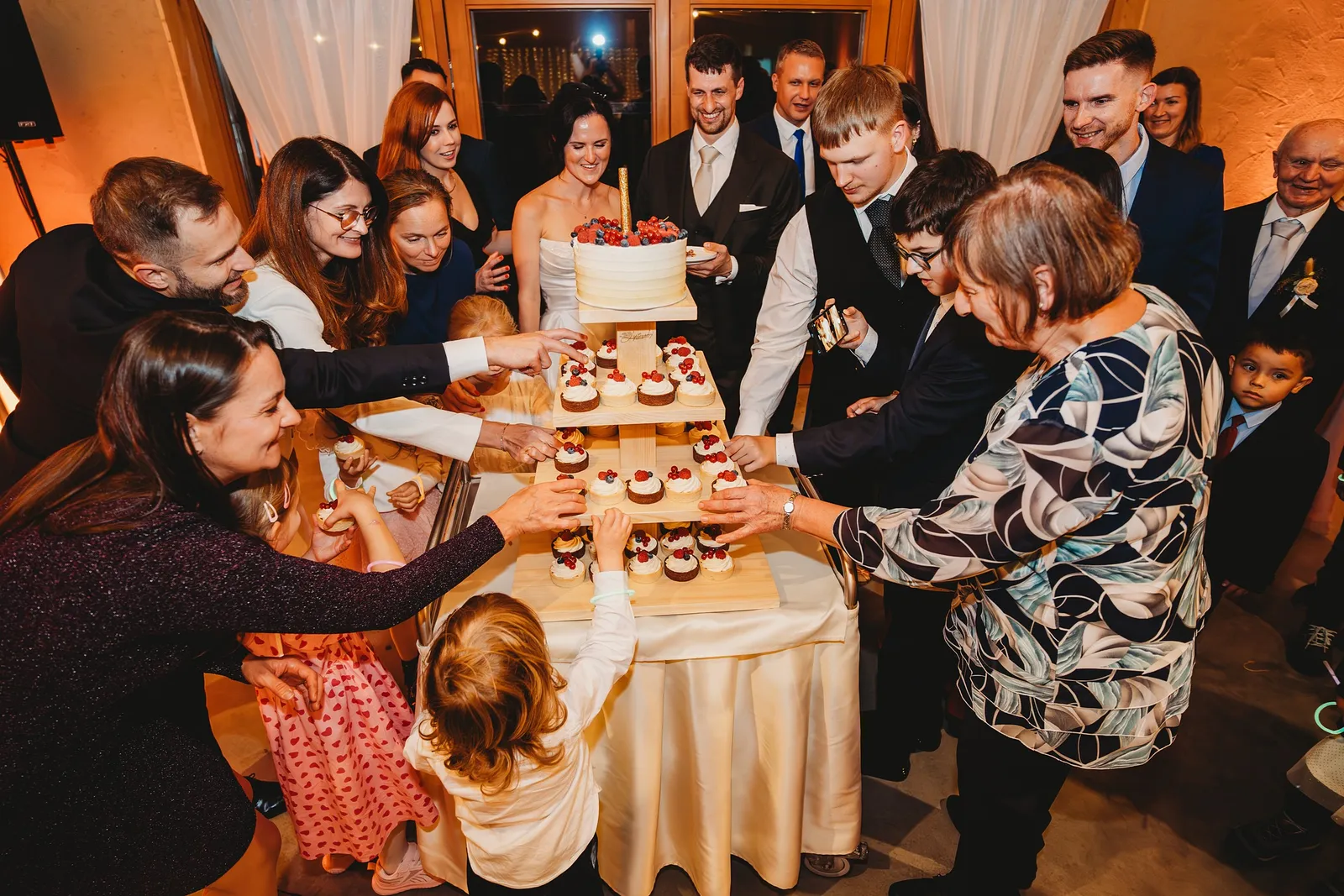 Hostia a deti si berú cupcakes z poschodového stojana so svadobnou tortou – svadba Andrejka a Janko, Stodola Liptovský dvor