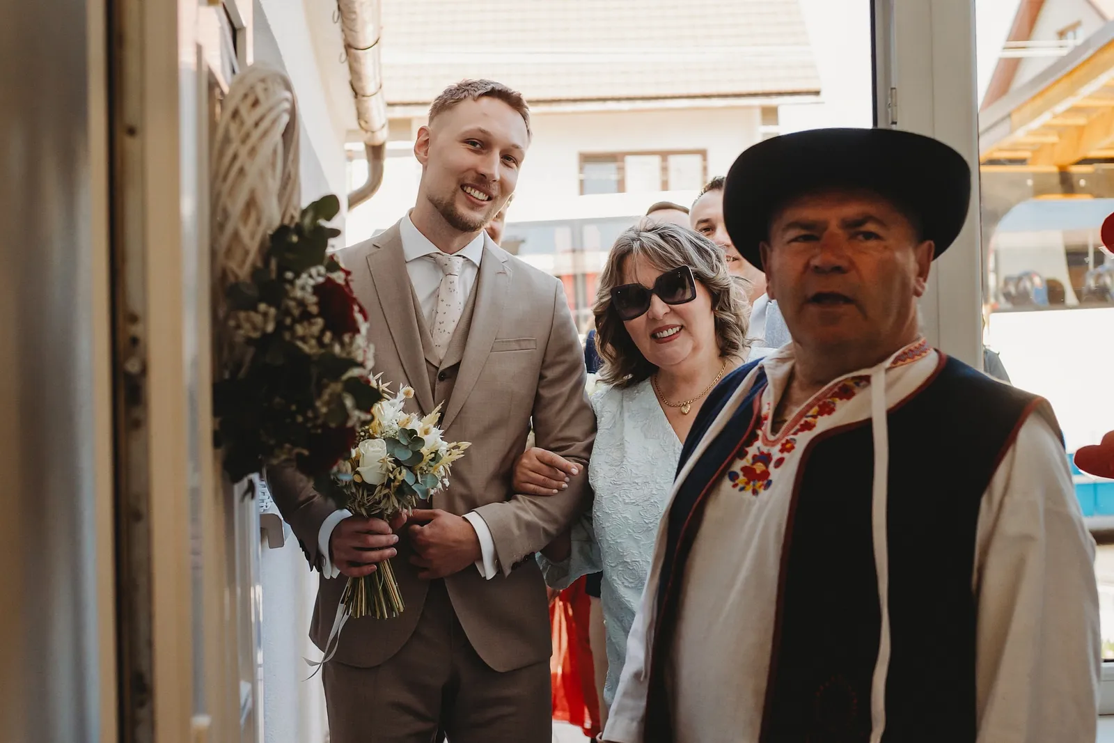 Ženích s kyticou a mamou prichádza po nevestu, vpredu ide muž v ľudovom kroji a klobúku – svadba Denisa a Martin, Stodola na poli