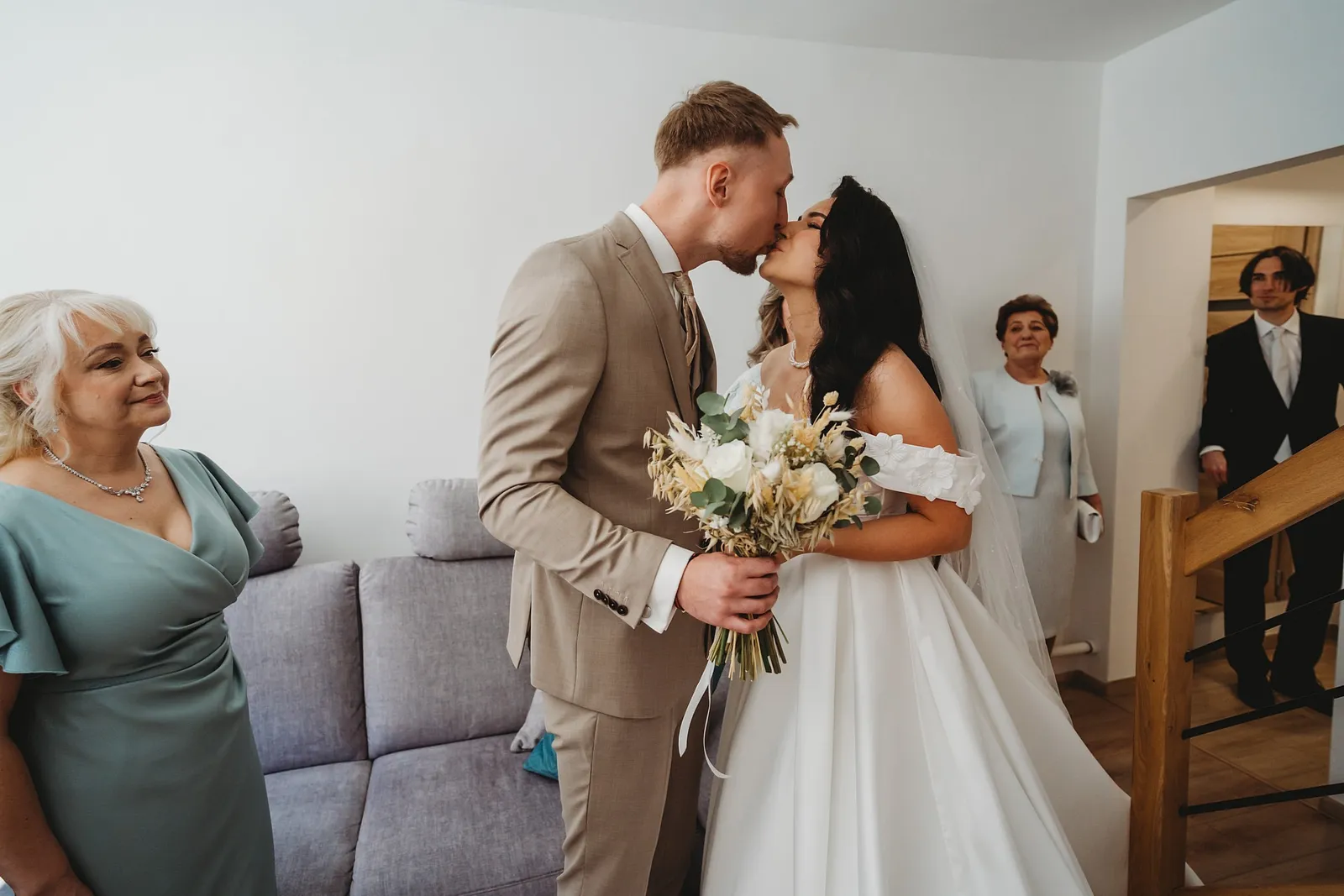 Ženích s kyticou bozkáva nevestu v obývačke, mama a rodina sa dojato prizerajú – svadba Denisa a Martin, Stodola na poli