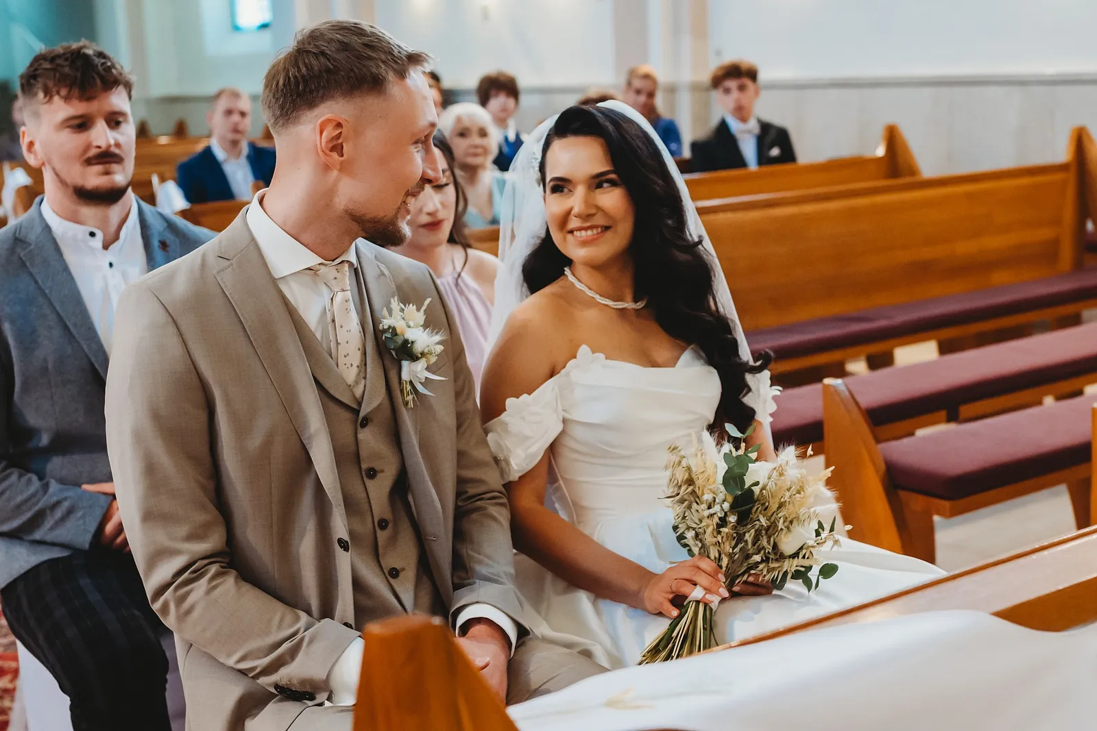 Nevesta s kyticou sa usmieva na ženícha, keď spolu kľačia pred oltárom v kostole – svadba Denisa a Martin, Stodola na poli