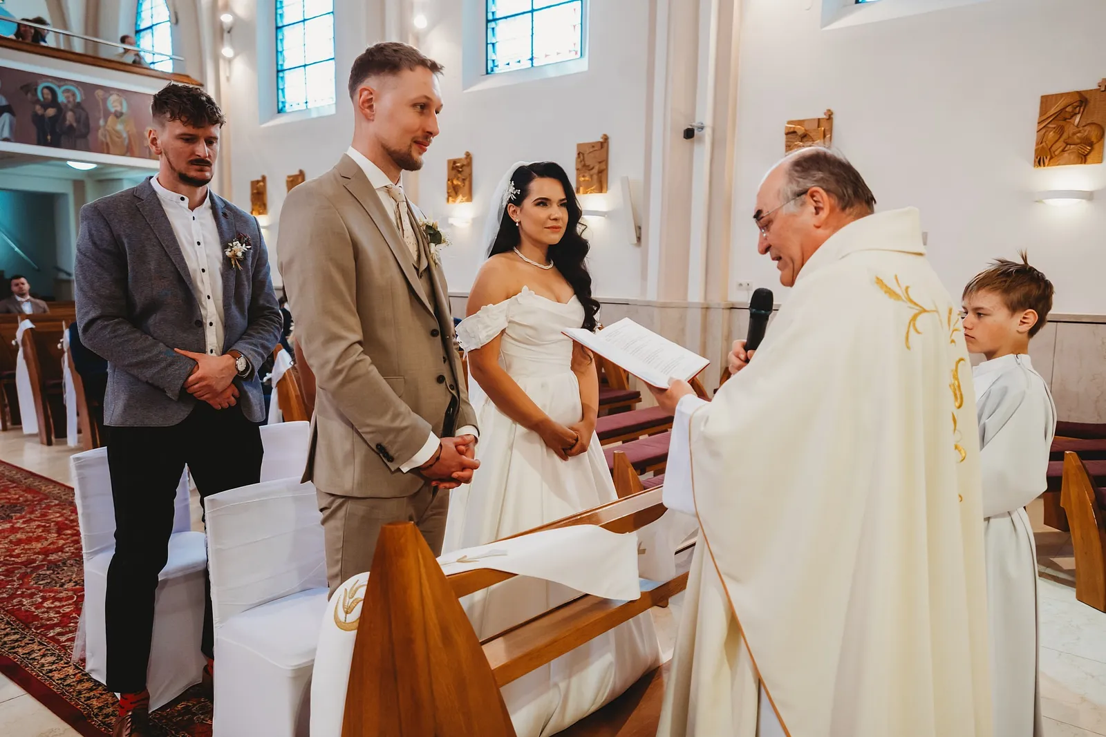 Kňaz číta zo svadobnej knihy, nevesta a ženích stoja pred ním so svedkom a miništrantom – svadba Denisa a Martin, Stodola na poli