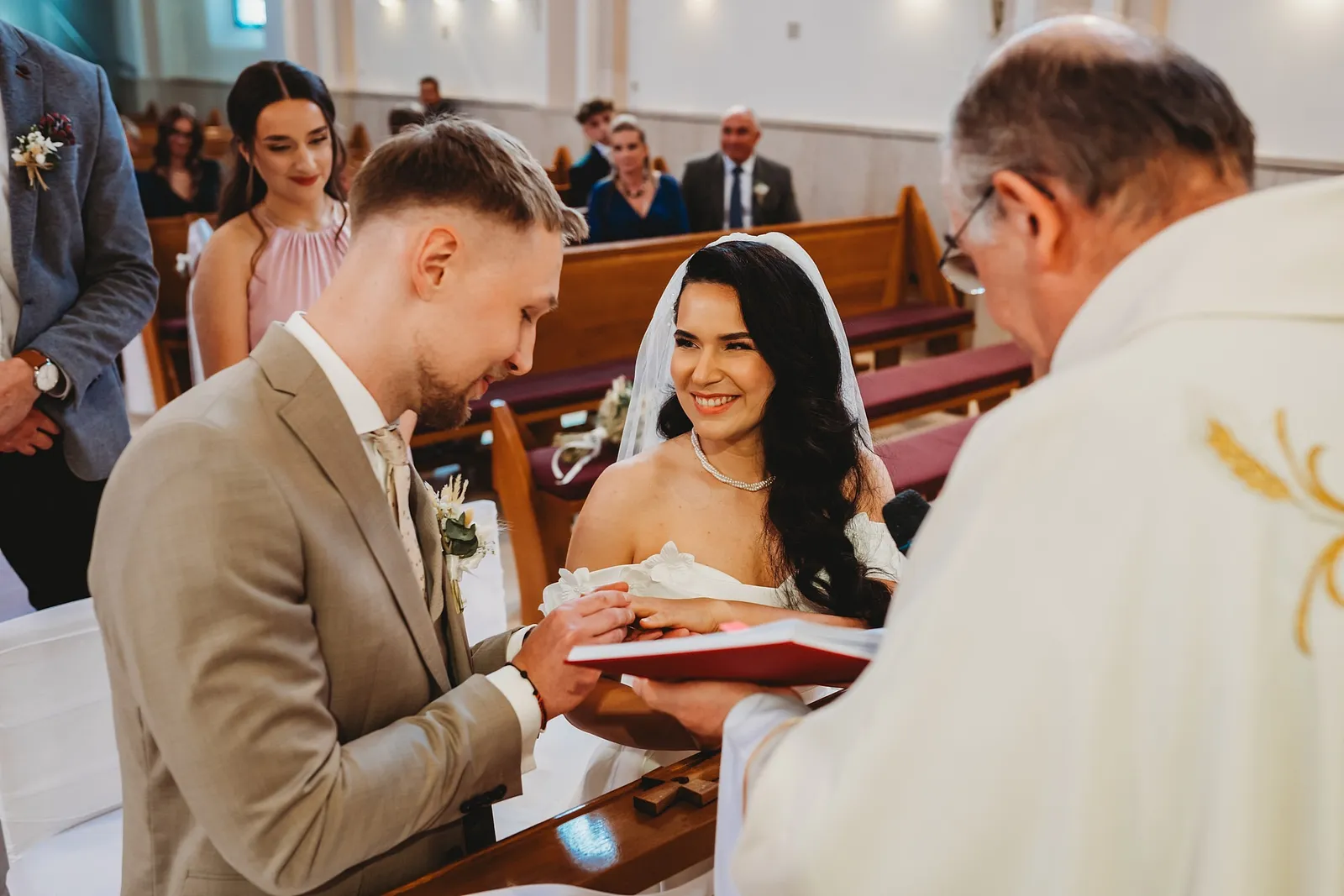 Nevesta a ženích kladú ruky na knihu, ktorú drží kňaz, počas manželského sľubu – svadba Denisa a Martin, Stodola na poli