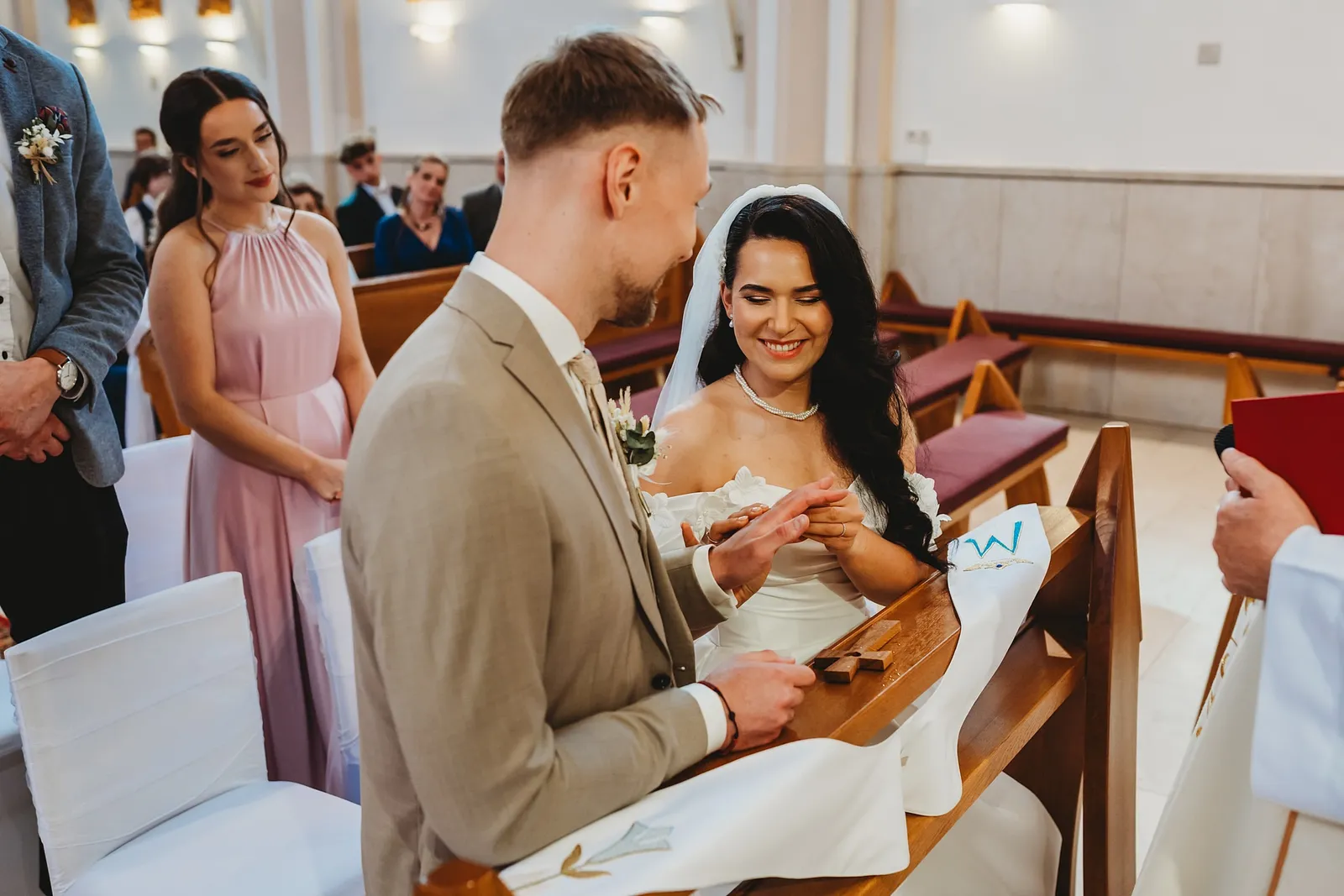 Ženích navlieka usmiatej neveste obrúčku pred oltárom, svedkyňa sa pozerá – svadba Denisa a Martin, Stodola na poli