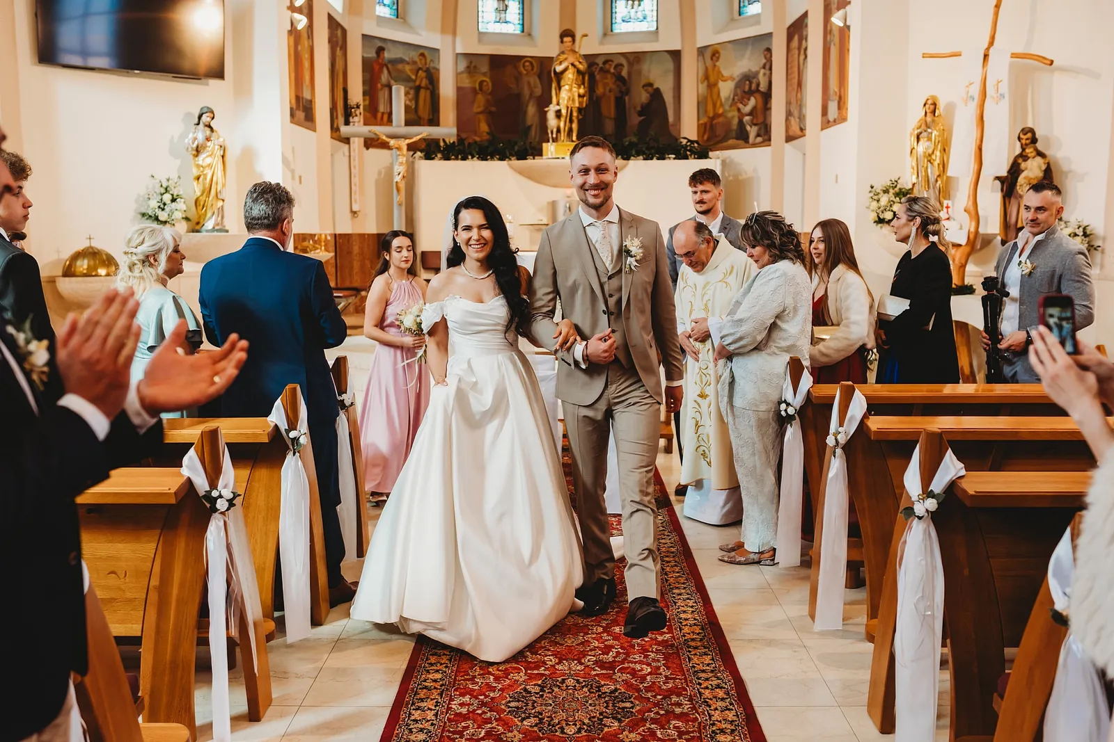 Novomanželia odchádzajú z kostola uličkou po červenom koberci, hostia tlieskajú – svadba Denisa a Martin, Stodola na poli