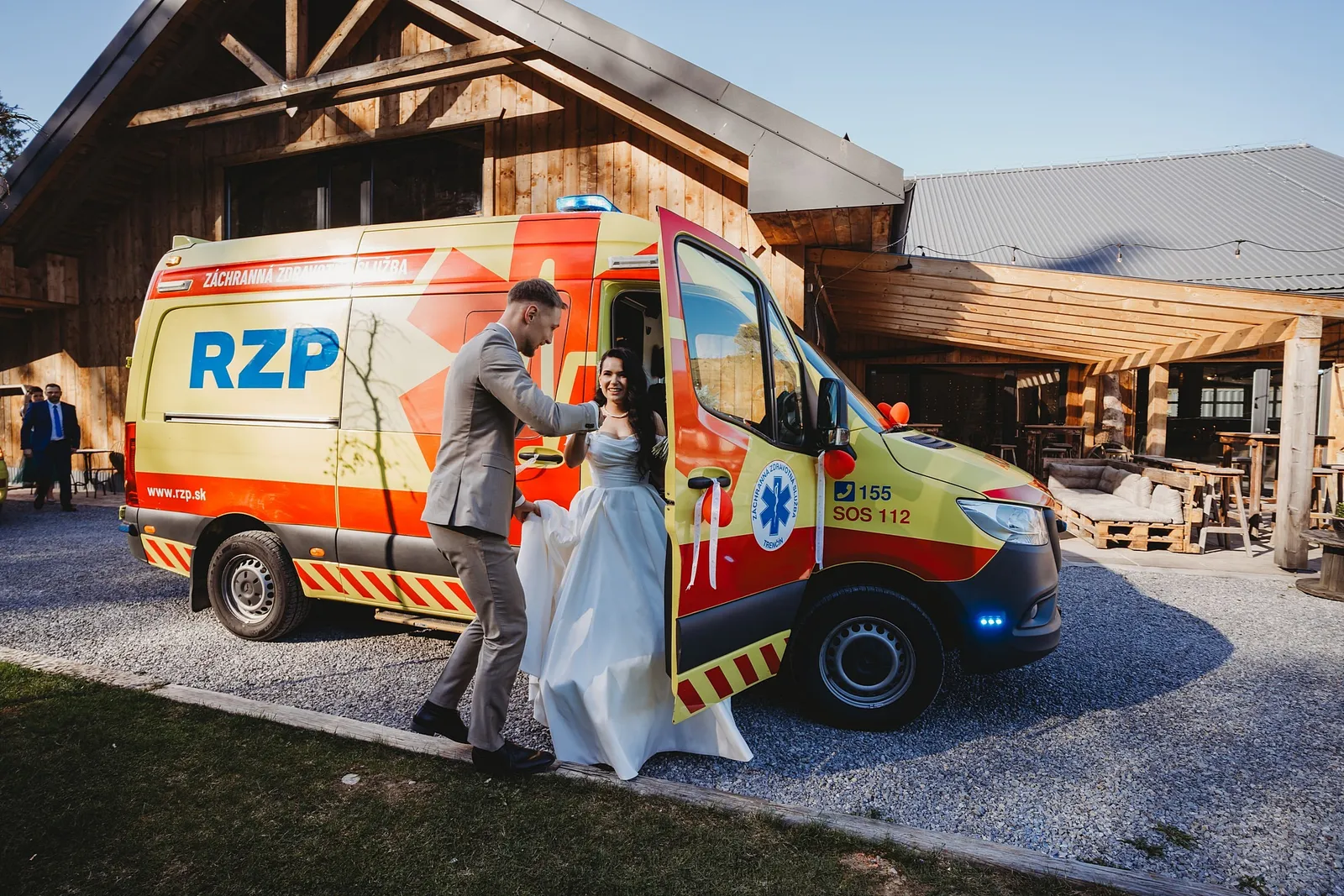 Ženích pomáha neveste vystúpiť zo žltej sanitky RZP pred drevenou stodolou – svadba Denisa a Martin, Stodola na poli