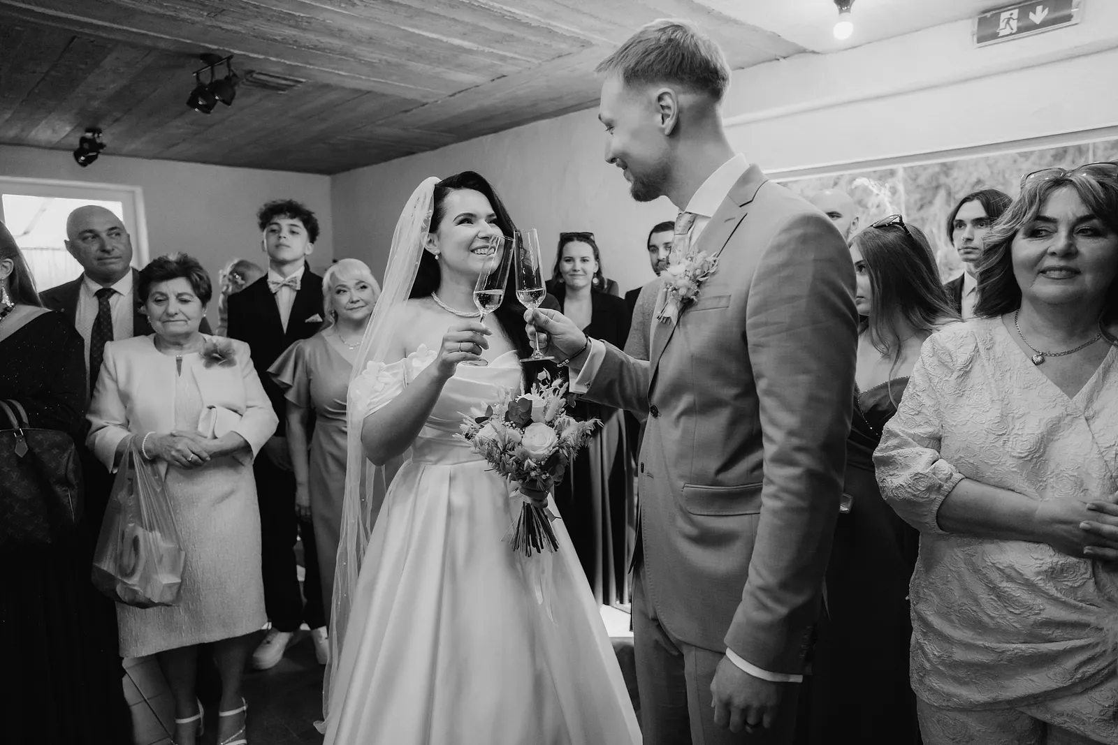 Čiernobiely prípitok nevesty a ženícha pri vstupe do sály obklopených hosťami – svadba Denisa a Martin, Stodola na poli