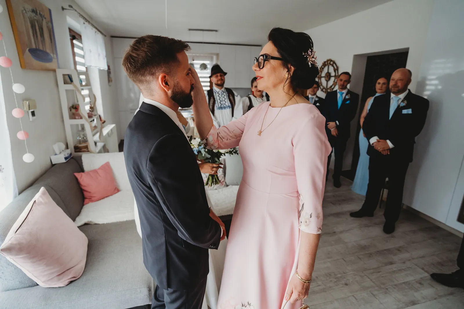 Mama nevesty v ružových šatách žehná ženíchovi dotykom na čele, hostia stoja v izbe – svadba Natália a Tomáš, Hotel Demänová