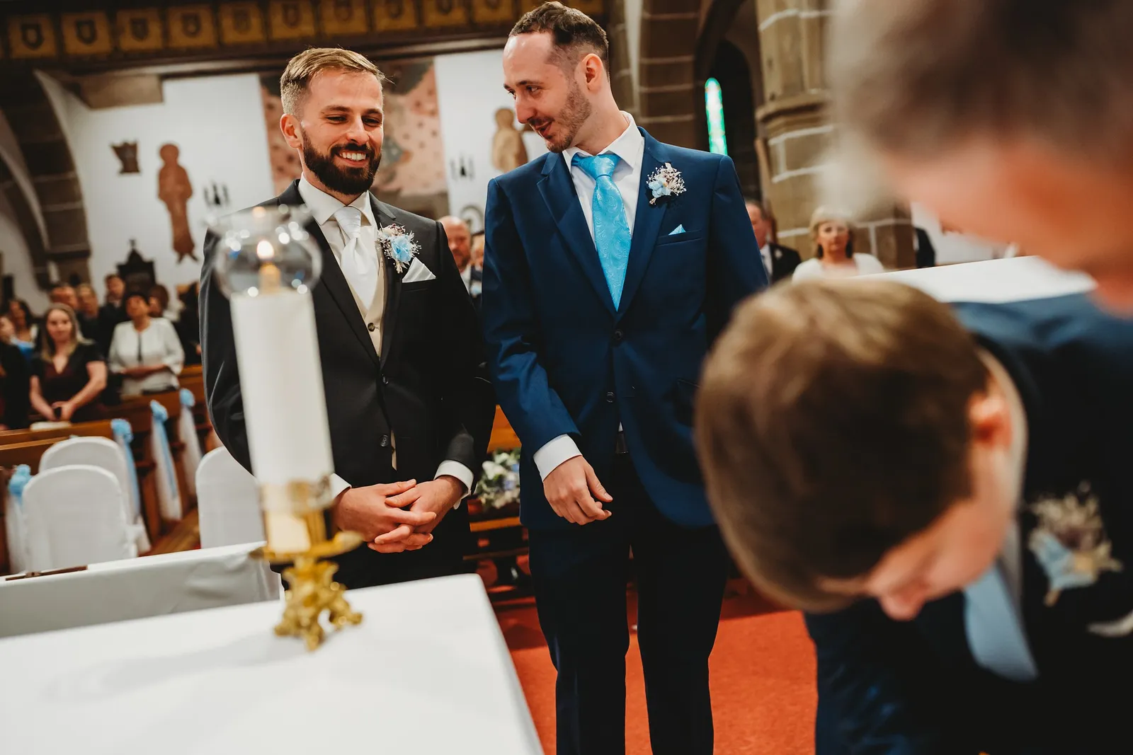 Ženích sa pri oltári smeje so svedkom v modrom obleku vedľa veľkej sviece – svadba Natália a Tomáš, Hotel Demänová