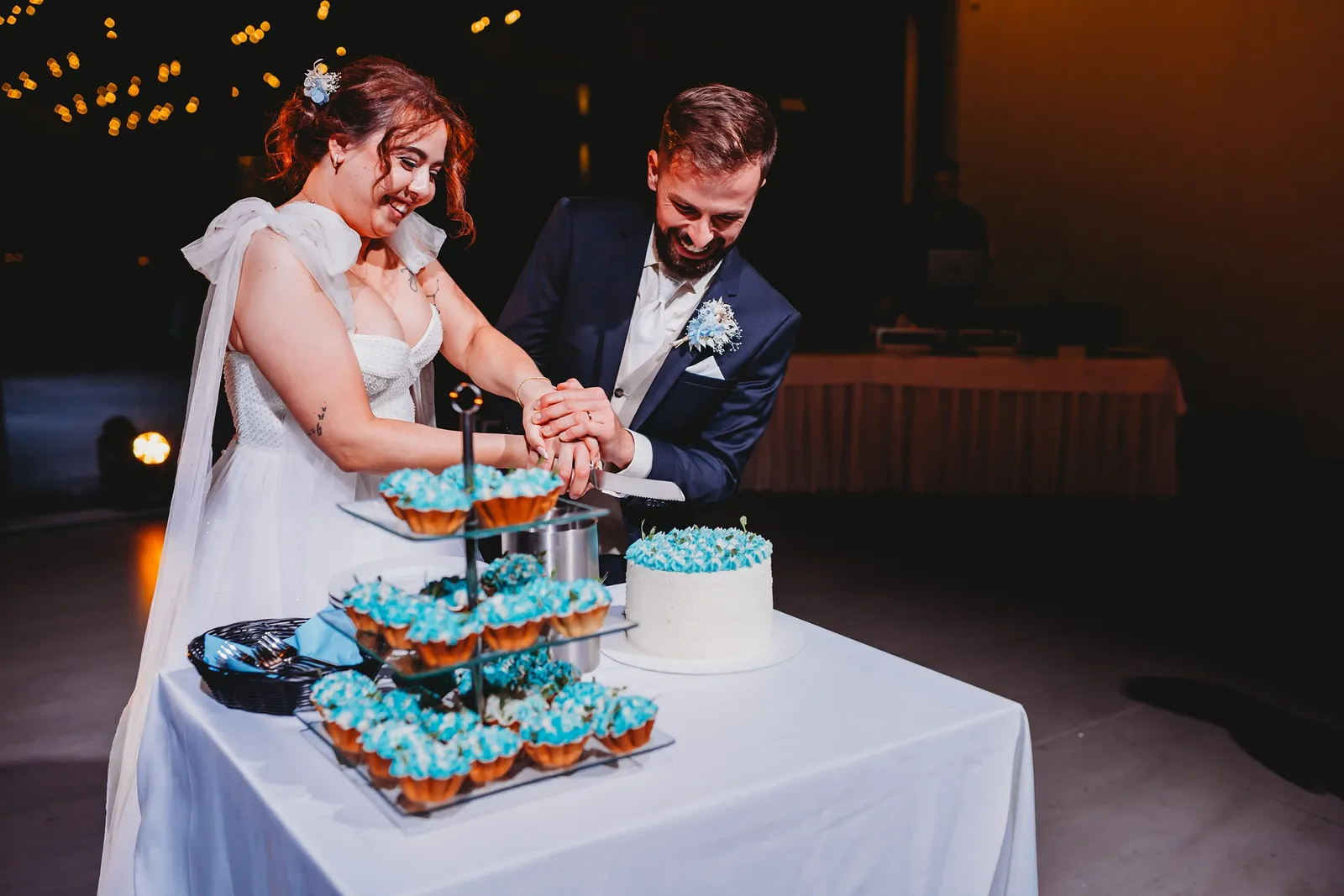 Novomanželia spoločne krájajú tortu s modrou ozdobou vedľa etažéra s cupcakes – svadba Natália a Tomáš, Hotel Demänová