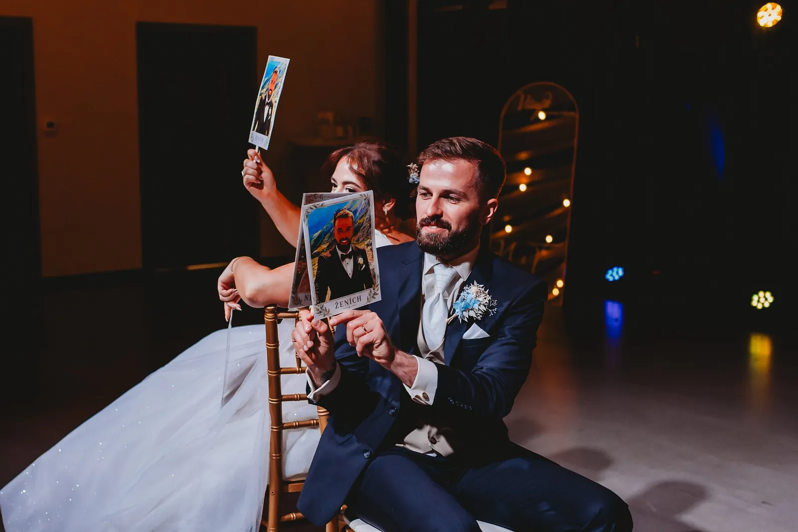 Nevesta a ženích na stoličkách dvíhajú fotky ako odpovede počas svadobnej hry – svadba Natália a Tomáš, Hotel Demänová