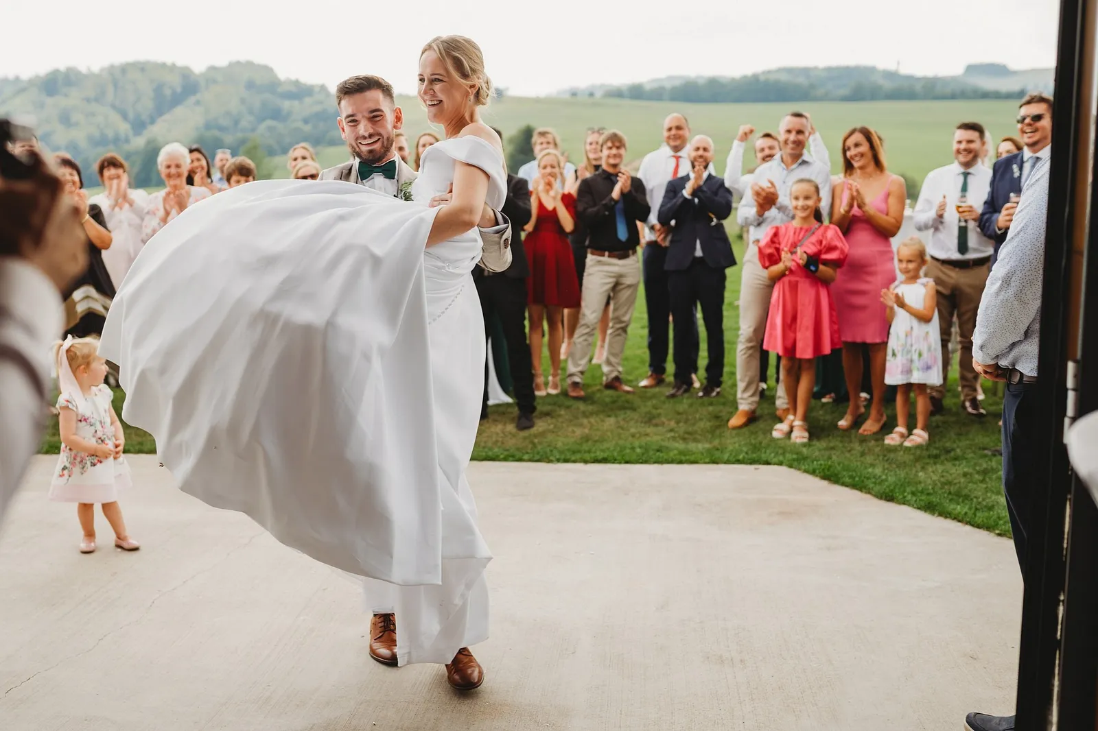 Ženích prenáša nevestu cez prah, hostia za nimi tlieskajú a smejú sa – svadba Veronika a Elior, Stodola Pohanské