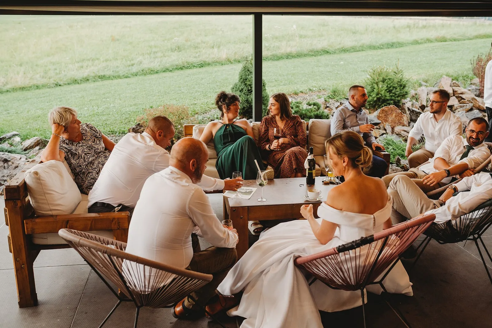 Nevesta posedáva s hosťami v lounge zóne pri veľkom okne s výhľadom na lúku – svadba Veronika a Elior, Stodola Pohanské