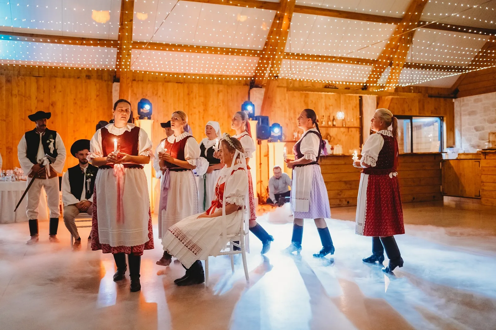 Folklórny súbor v krojoch spieva pri čepčení nevesty so sviečkami v rukách – svadba Veronika a Elior, Stodola Pohanské