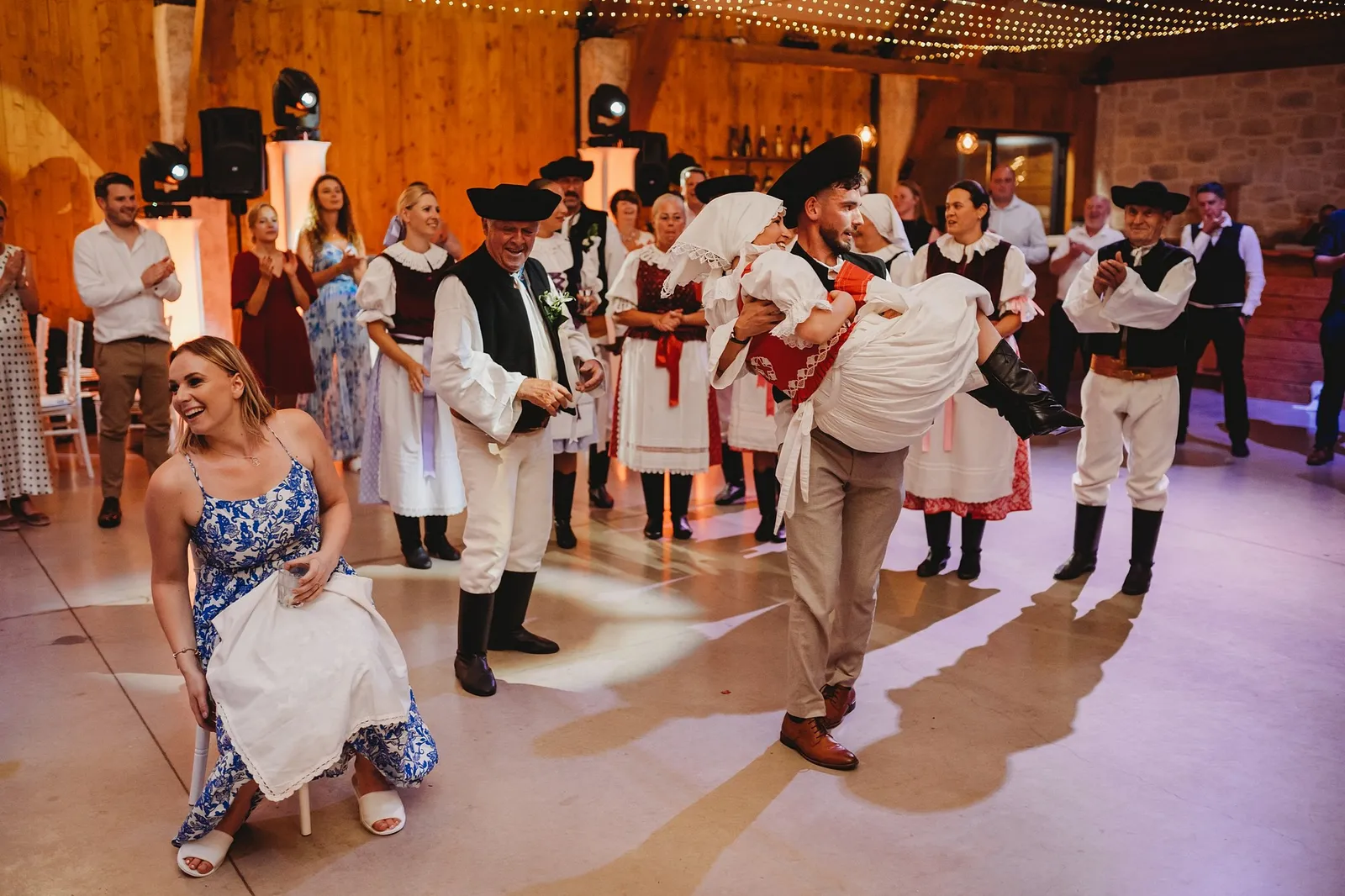 Tanečníci v krojoch a ženích nesie nevestu v čepci na rukách pri polnočnom programe – svadba Veronika a Elior, Stodola Pohanské